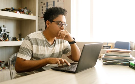 A teenage boy studies on his laptop computer at home.