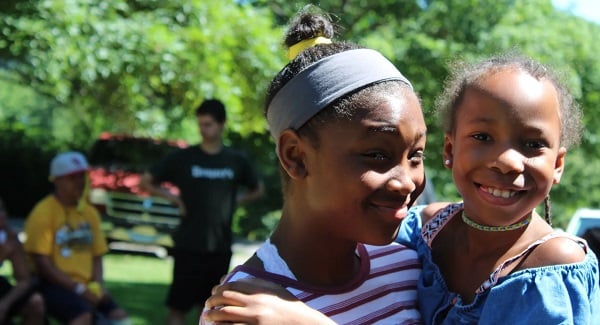 Two girls hug and smile as other kids play in the background