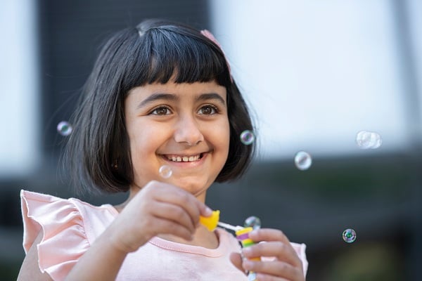 A girl wearing a pink shirt and pink bow blows bubbles in the Healing Garden at Children's National Hospital.