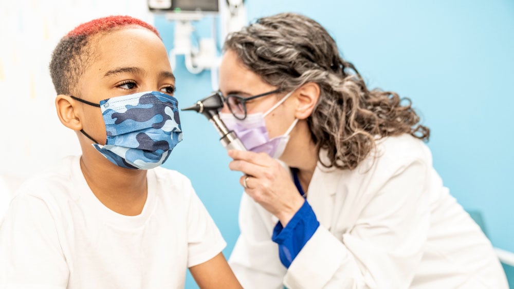pediatrician examinating young boys ear, both individuals are wearing masks