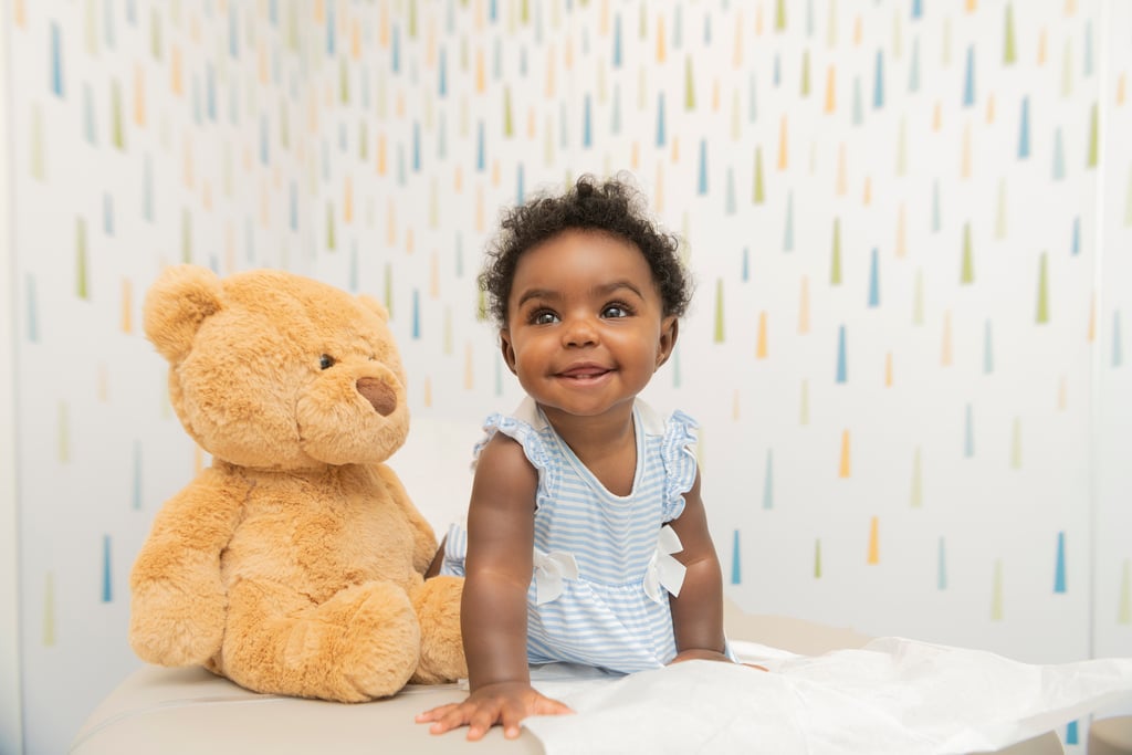 Smiling baby seated next to a large teddy bear