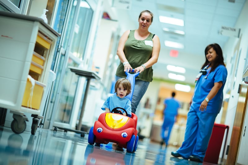 parent pushing child in toy car in hospital