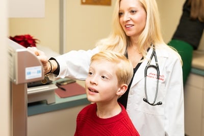 A boy in a red sweater stands on a scale as he is measured by a doctor.