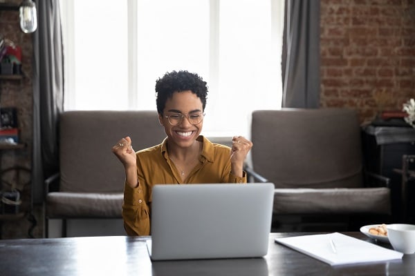 A woman clenching her fists and smiling whilelooking at her laptop