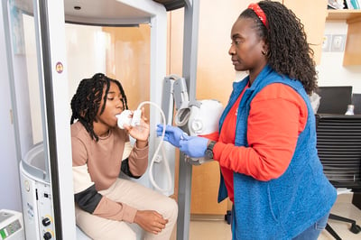 A nurse in the Advanced Lung Disease Program at Children's National Hospital holds a breathing test device up to a teen patient's mouth as he inhales for the test.