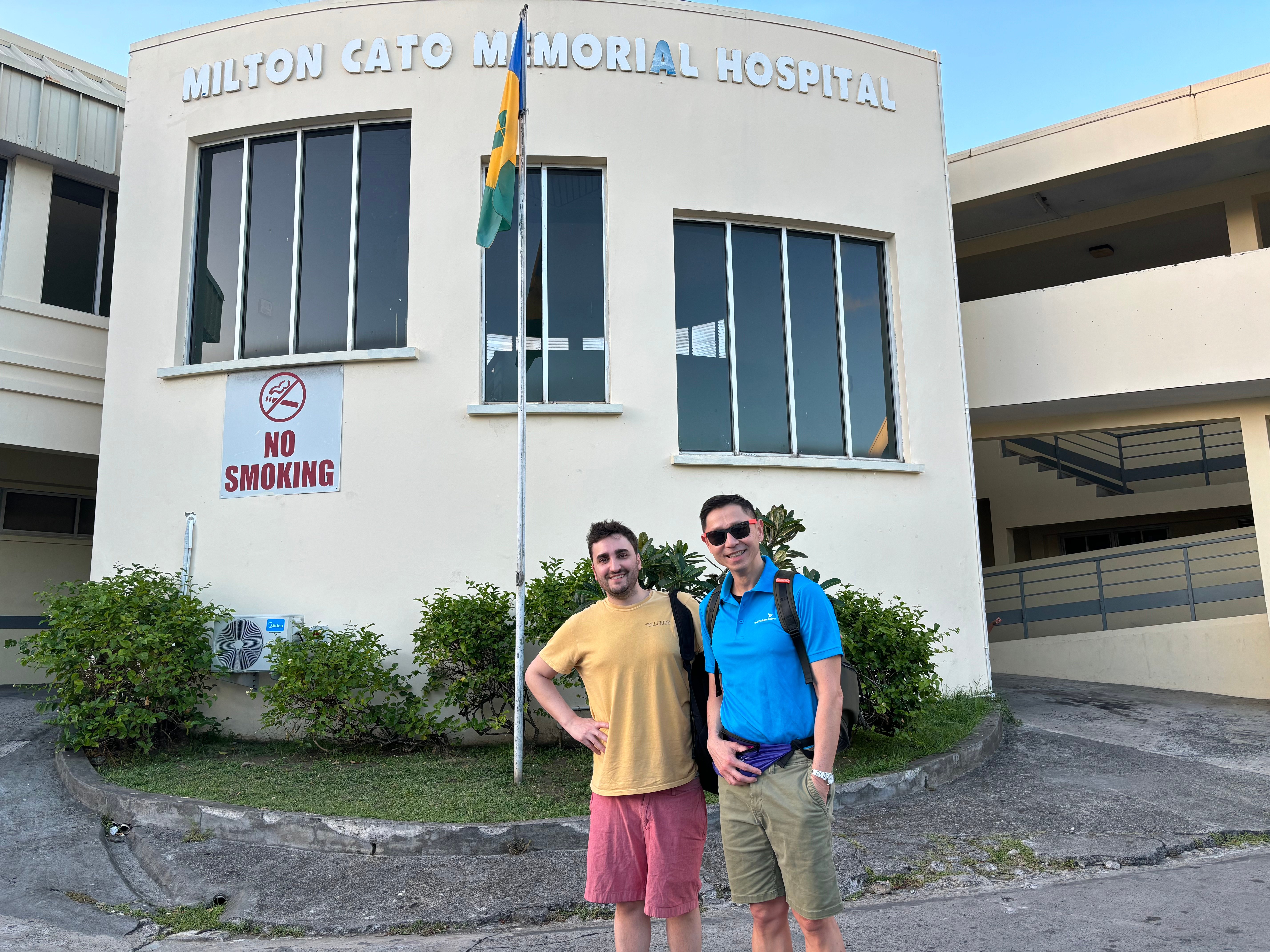 Two fellows pose in front of a hospital