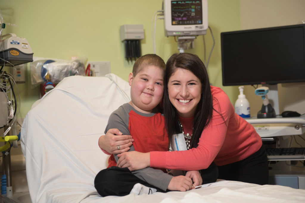 Boy on hospital bed getting hug from smiling woman.