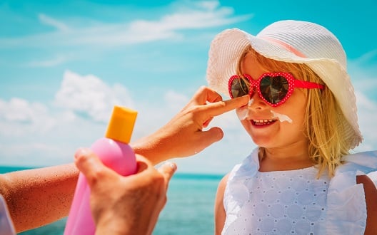 A mom applies sunscreen to her daughter's face at the beach