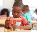 African American boy working with wooden shapes while sitting at a desk