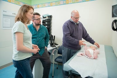 Dr. Marc Levitt holds the hand of a baby on an exam table.