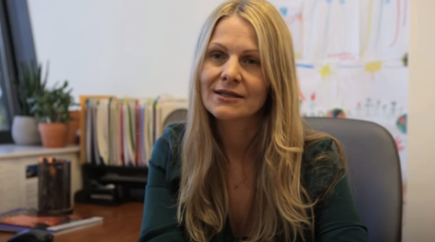 Screenshot of a video. Catherine Limperopoulos has long blond hair and is sitting at a desk.