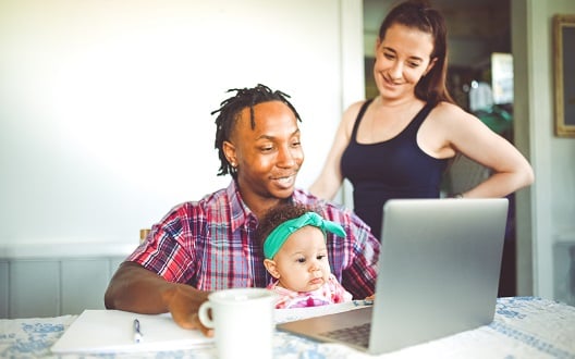 A family of three looks at a laptop computer while smiling.