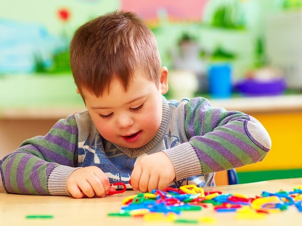 A boy sits at a table playing with colorful plastic chain link toys.