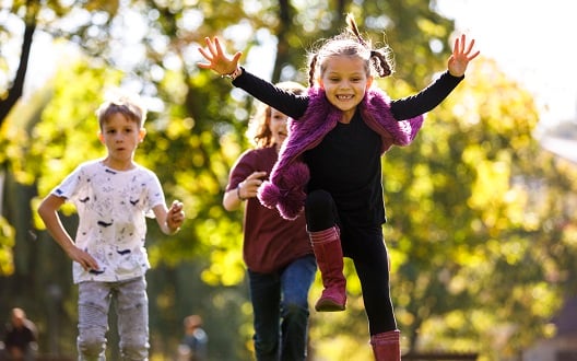 Two girls and a boy run outside on a sunny day