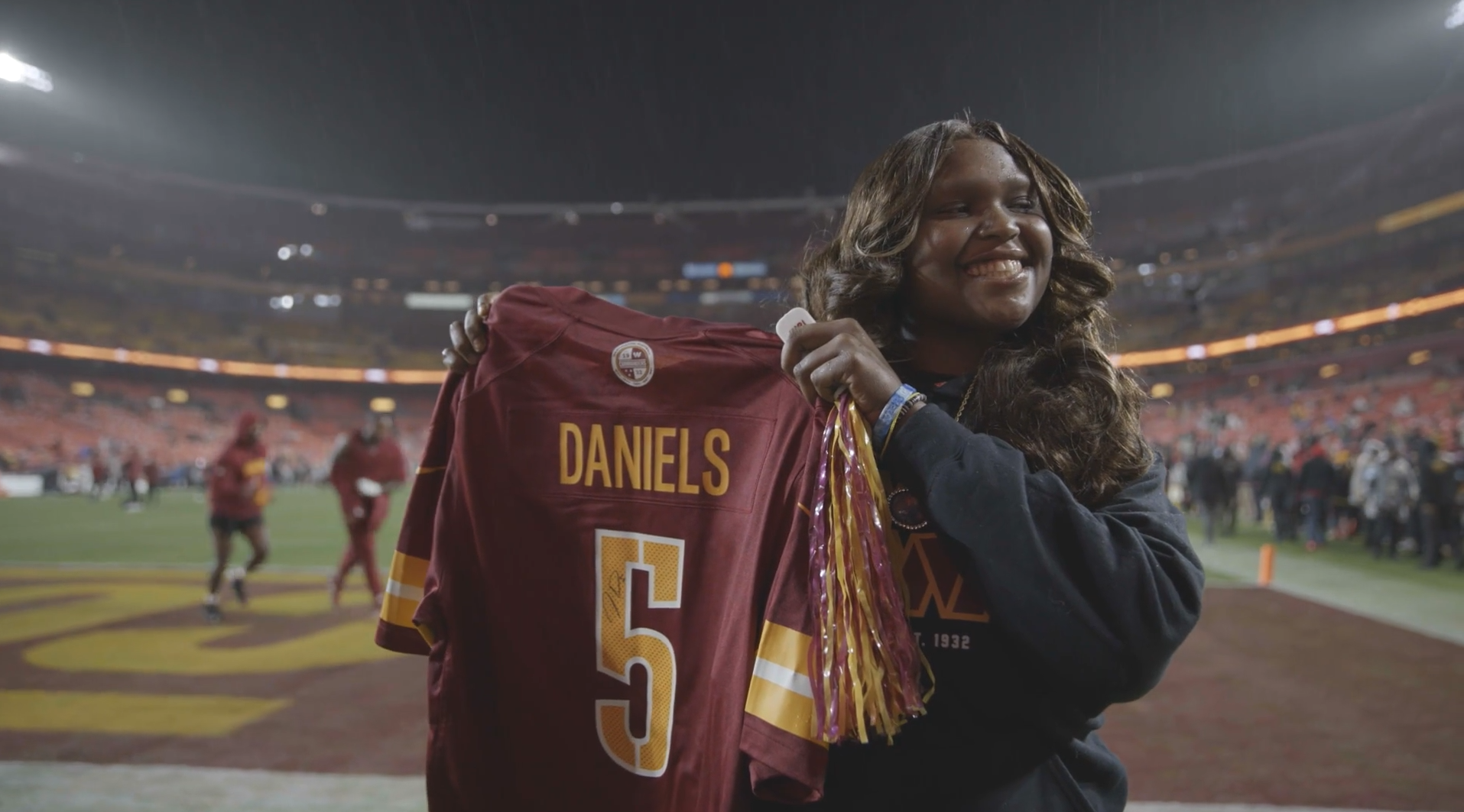 Children's National patient Sarah Addison holding signed Jayden Daniels jersey on the sidelines at a Washington Commanders game