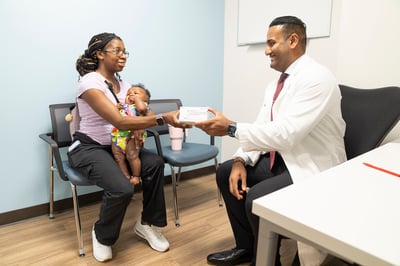 A mother holds her baby while receiving a prescription from a pharmacist at Children's National Specialty Pharmacy