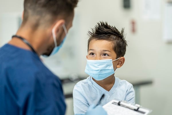 A boy and a nurse, both wearing masks, look at each other during an appointment.