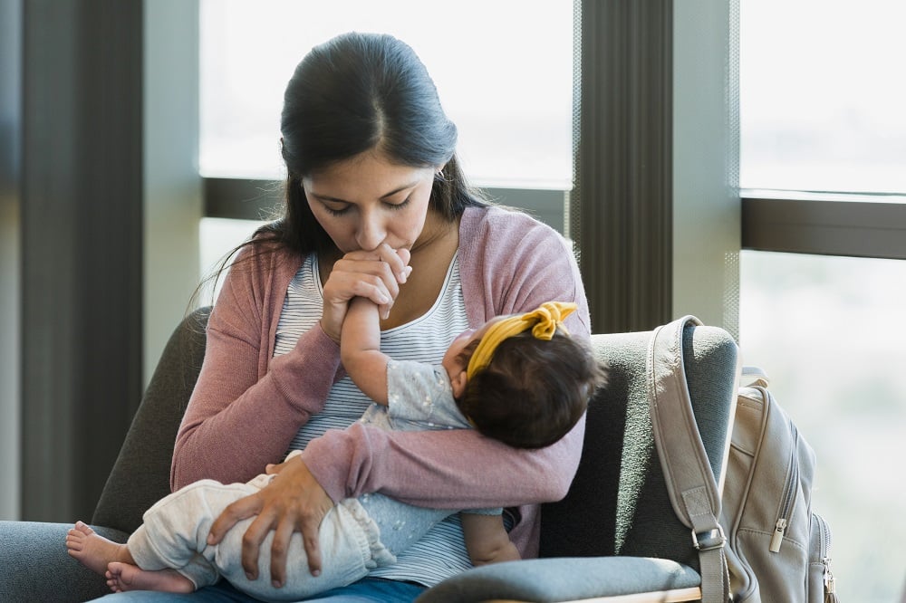 A mother cradles her baby in her arms while she kisses her baby's hand.