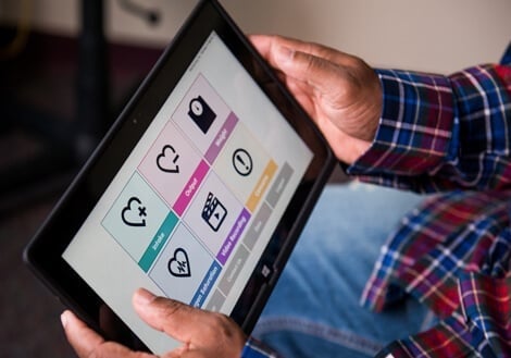 A caregiver looks at a tablet with a home monitoring app after their child's heart surgery.