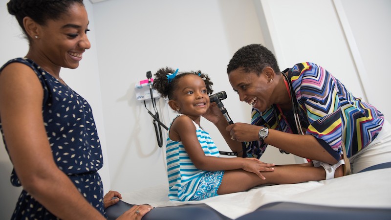 Smiling girl on exam table getting her ears checked by a female doctor