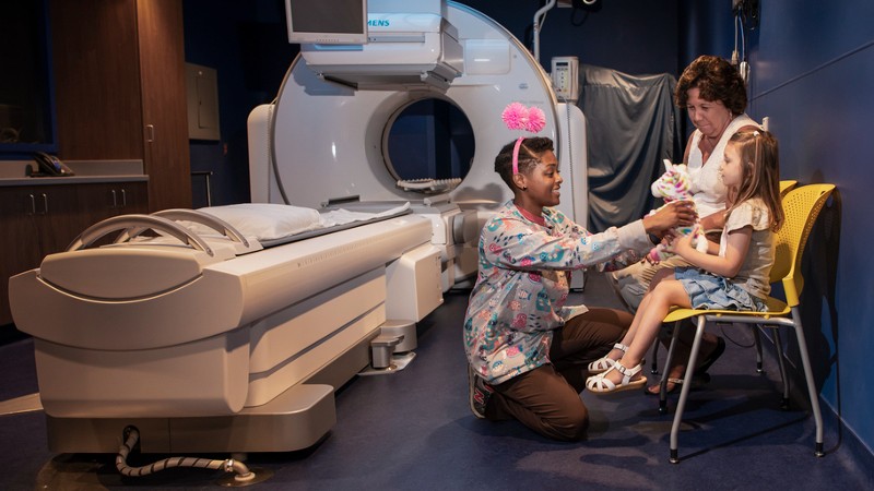 Enfermera dando niña un animal de peluche en la sala de imágenes de resonancia magnética