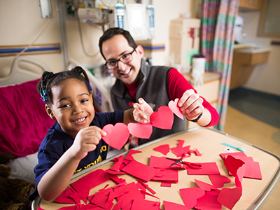 girl in hospital bed cutting paper hearts