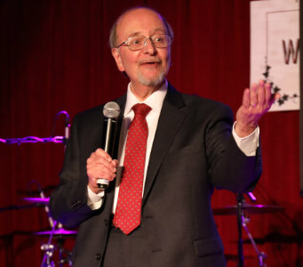 Lawrence D'Angelo, M.D., holds a microphone on stage while speaking.