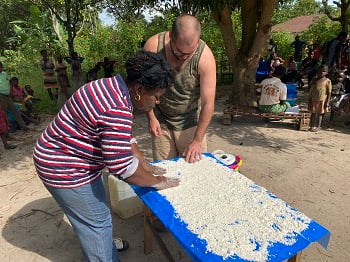 A man and woman spread cassava flour on a tarp to wet it and dry it to release toxins from it before eating.