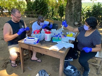 Three researchers sit at a table working on samples for their study.