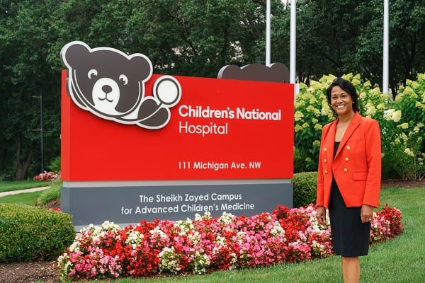 Children's National President and CEO Michelle Riley-Brown next to the main hospital front entrance sign.