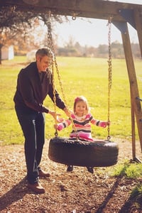 father pushing little girl on a tire swing