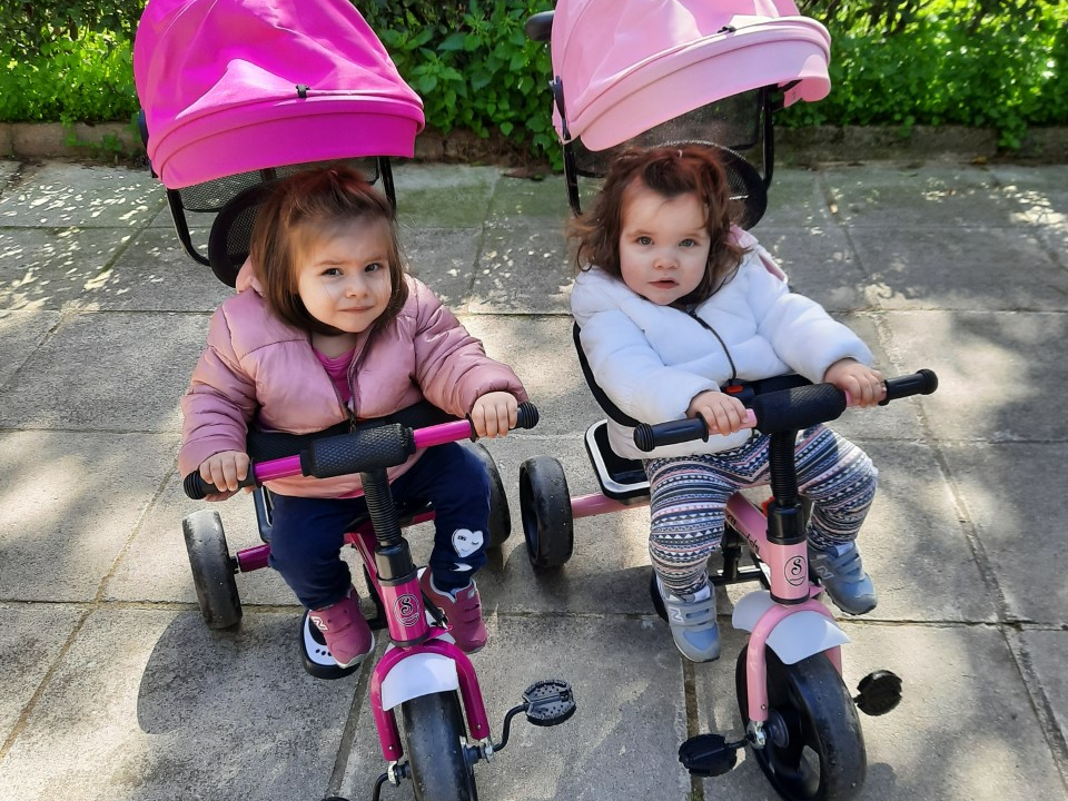 Stella and her sister riding tricycles