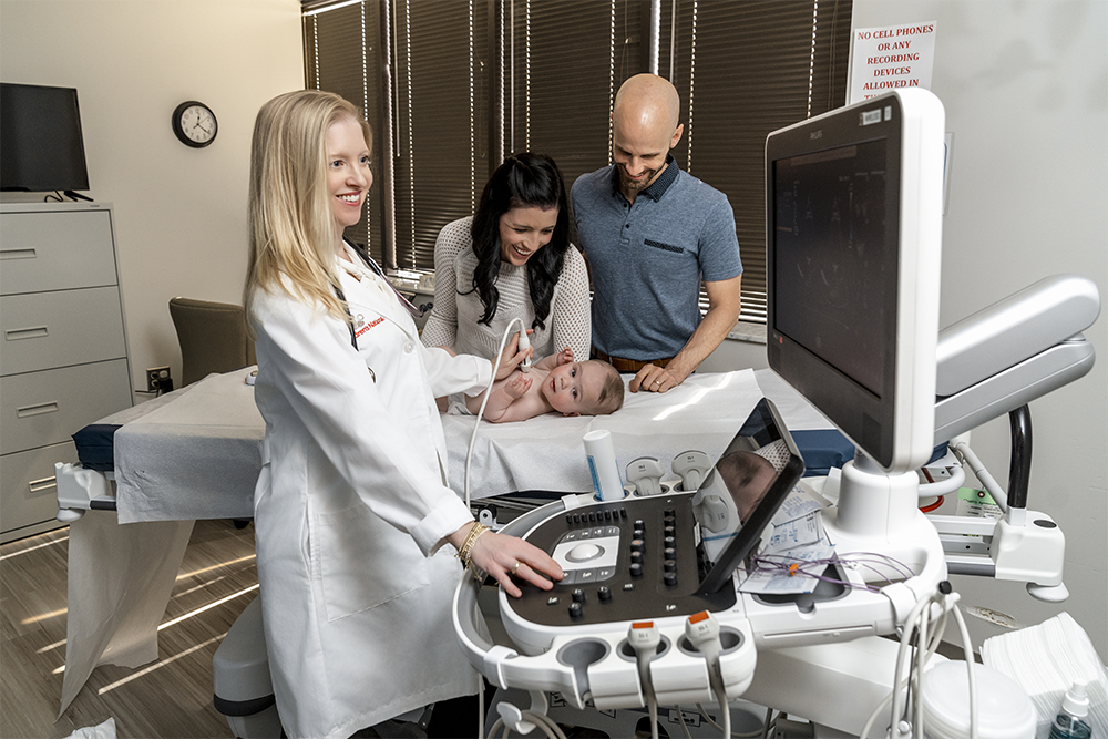 Doctor with parents and baby, giving baby an ultrasound of their heart.