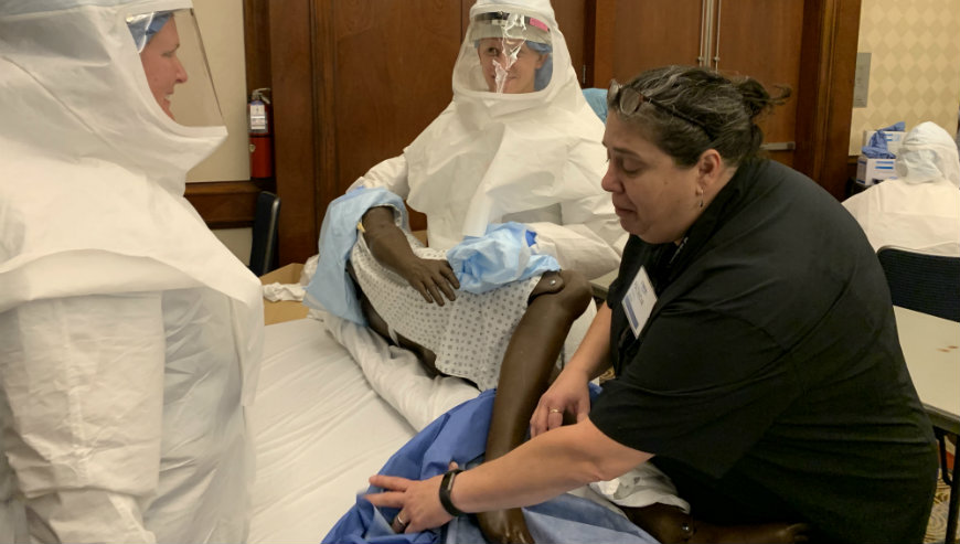 Ebola training team works together over practice patient.