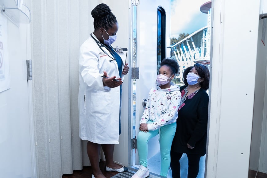 A doctor greets a mother and daughter entering the mobile health van.