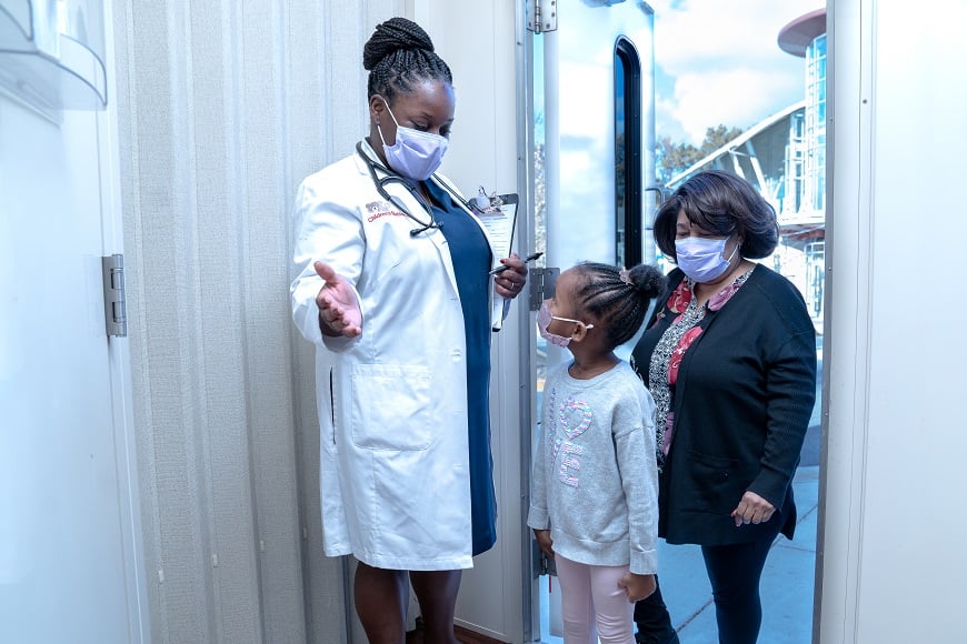 A doctor greets a mother and daughter in the mobile health van.