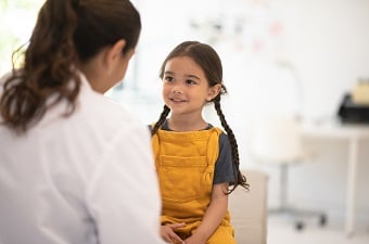 Girl in yellow overalls sitting on exam table