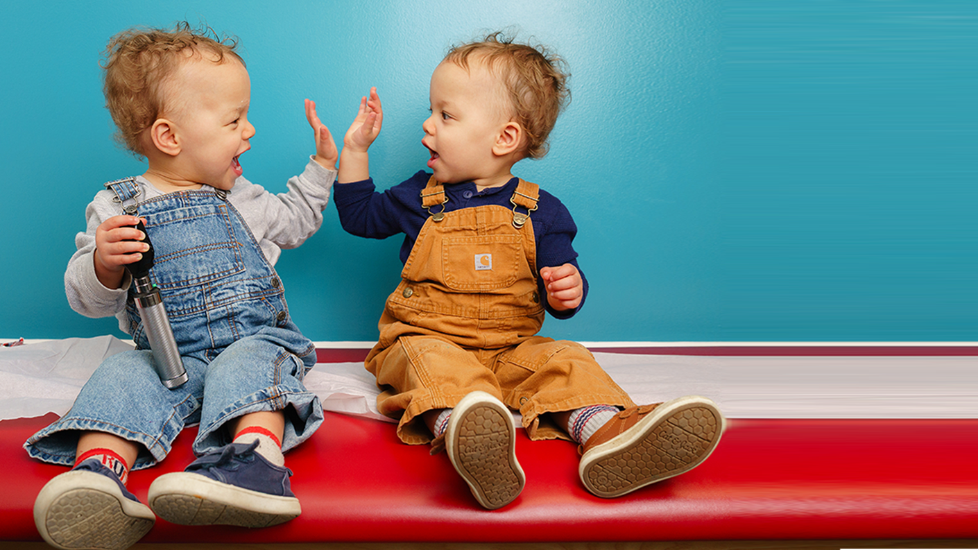 two toddlers high-fiving on exam table