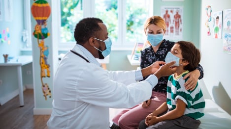 Pediatrician checking young boy with mom looking on