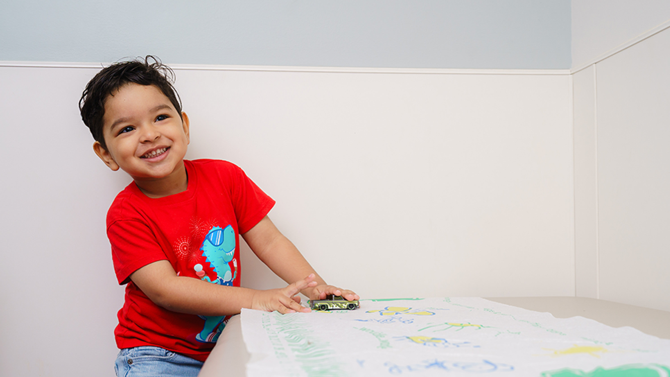 smiling boy playing with a racecar on exam table