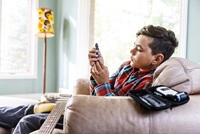 A boy sits on a couch with a guitar in his lap as he tests his own blood sugar level.