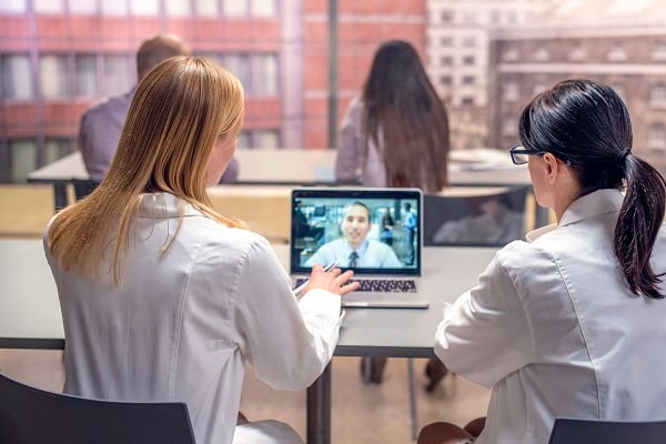 Two female health care providers watch a web conference on a laptop.