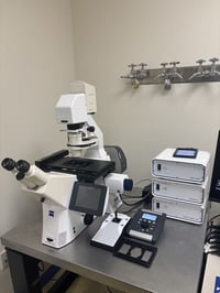 White and black inverted microscope. White control units stacked on right side of microscope.