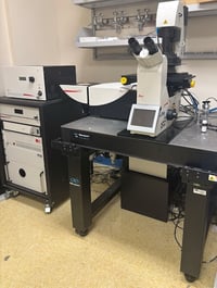 Black and white confocal inverted stand, on top of air table. Control and laser unit on the left on microscope.