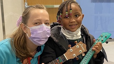 A female music therapist and little girl smile for a photo while holding guitars