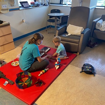 A music therapist sits on a red mat with a child for a music session at Children's National Hospital