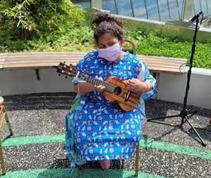 A young girl plays a ukulele while sitting in the Healing Garden