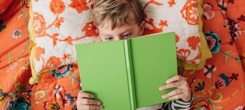 A little boy reading a book with a green cover