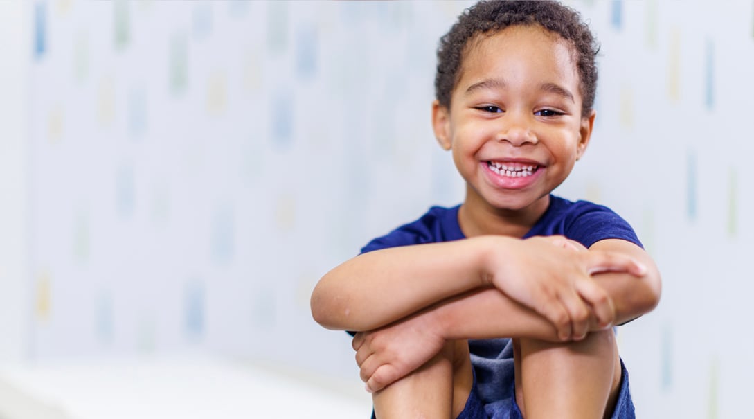 A young Black male patient smiles in an examination room.