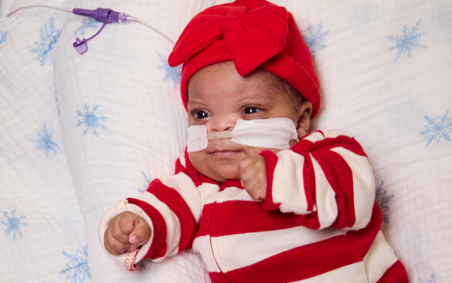 An infant patient in a red and white striped onesie lies on a blanket featuring blue snowflakes